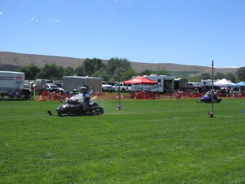 1981 Ford Bronco - A snowmobile is in motion on a grassy field during an outdoor event with spectators and trailers present.