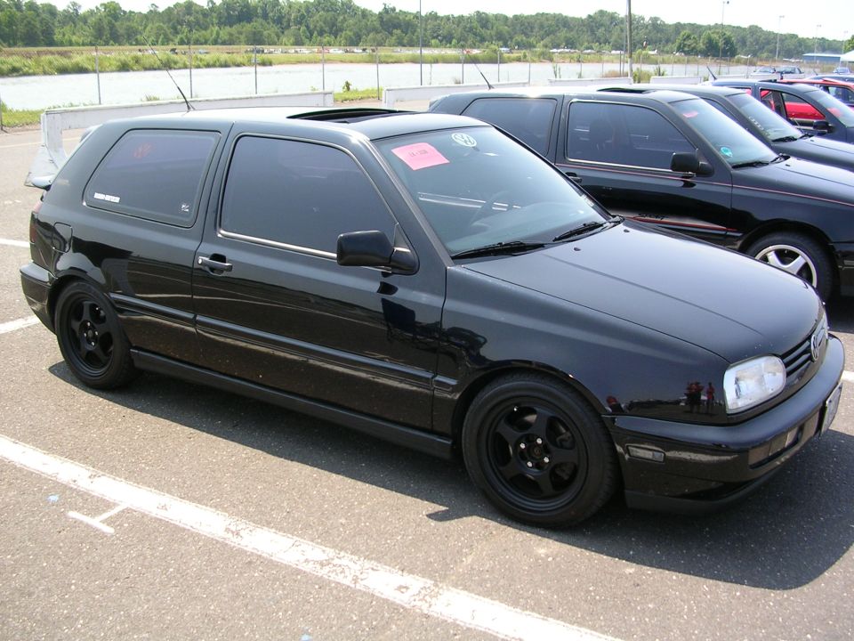 Black Volkswagen Golf GTI with aftermarket wheels and spoiler, parked in a lot
