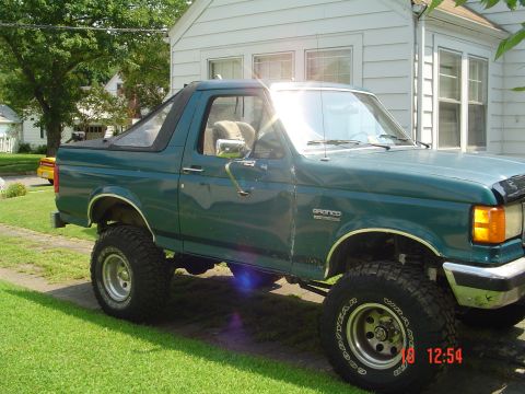 1989 Ford Bronco - A green 1989 Ford Bronco is parked on a lawn in front of a white house.