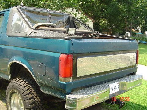 1989 Ford Bronco - Rear view of a teal SUV a soft top and diamond plate accents on the tailgate and bumper.