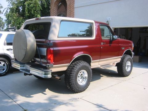 1996 Ford Bronco - This lifted Ford Bronco is parked in front of a garage, with a spare tire mounted on the rear.