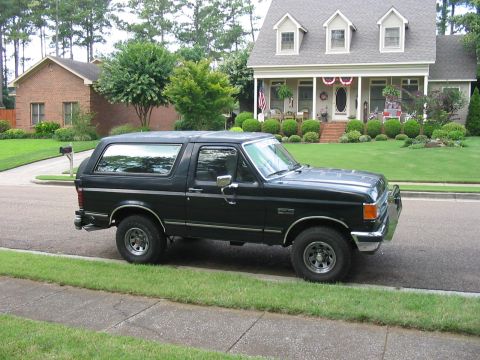1988 Ford Bronco - This black 1988 Ford Bronco is parked on the street in front of a well-maintained suburban home.