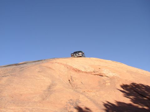 1996 Ford Bronco - A dark Ford Bronco navigates a steep, rocky terrain under a bright blue sky.