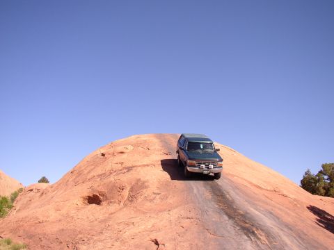 1996 Ford Bronco - A green SUV navigates a challenging off-road path on a large rock formation.