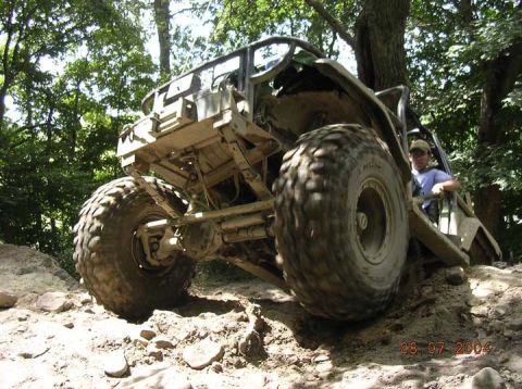 1992 Ford Bronco - A person sits in a heavily modified off-road vehicle navigating a rocky, wooded terrain.