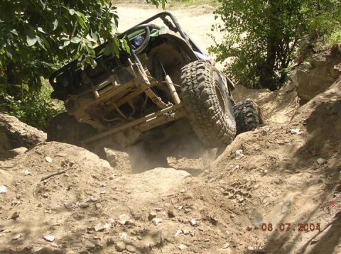 1992 Ford Bronco - Off-road vehicle tackling a challenging dirt climb with significant dust kicked up.