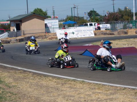 1990 Ford Bronco - Several go-karts are competing on a paved track with spectators in the background.