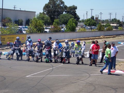 1990 Ford Bronco - Mini bikes and riders line up at the start of a race on a paved track.