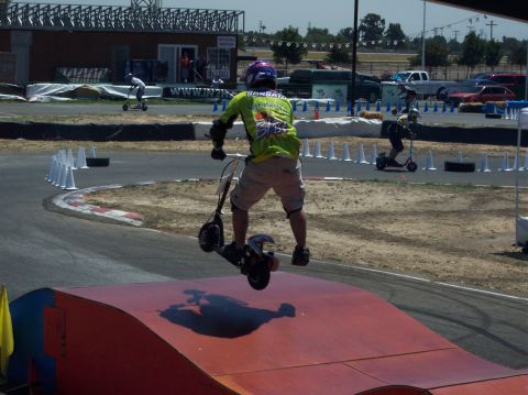 1990 Ford Bronco - Rider performs a jump on a scooter at a race event, with other participants visible.
