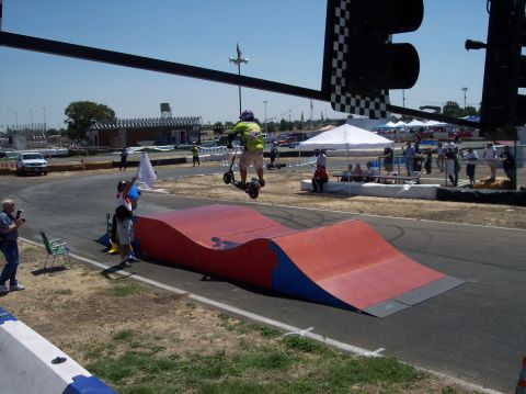 1990 Ford Bronco - A scooter rider performs a jump over a ramp at an outdoor event with spectators and tents in the background.