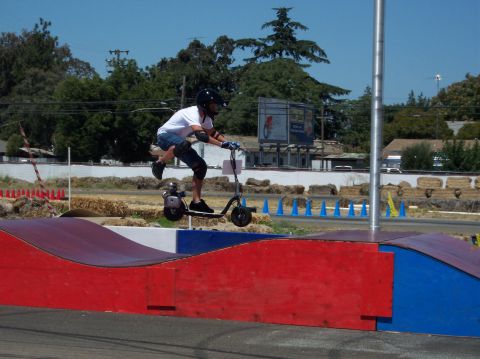 1990 Ford Bronco - Rider on a motorized scooter performs a jump over a ramp at an outdoor track.