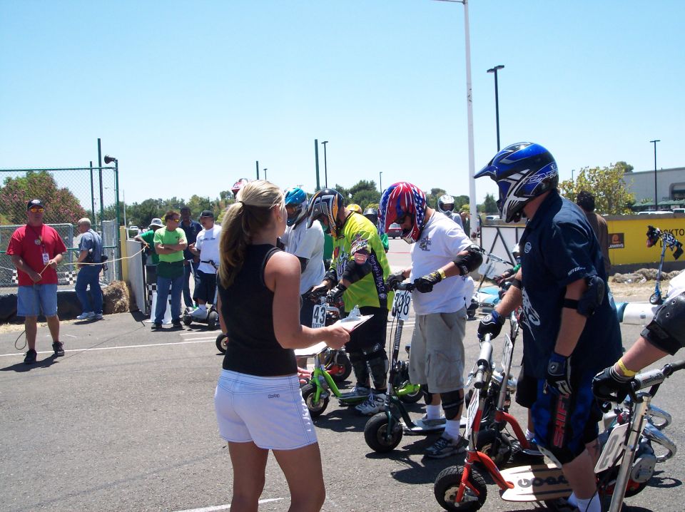 People in helmets line up with mini scooters for a race