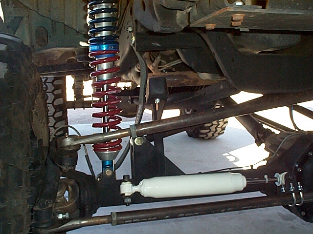 Custom front coilover suspension with red spring, steel links, and white steering stabilizer under a lifted truck