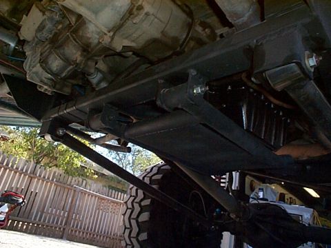 1994 Ford Bronco - The underside of a vehicle is shown, focusing on the transmission and suspension parts. A large tire is visible on the right.