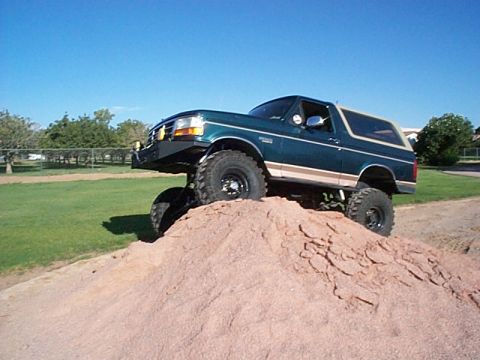 1994 Ford Bronco - This lifted Ford Bronco is shown climbing a dirt pile under a clear blue sky.