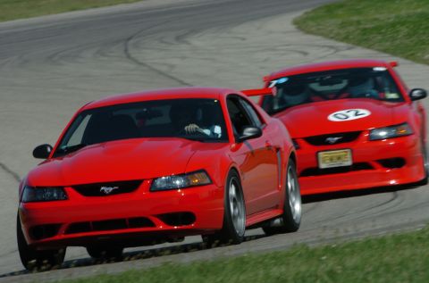 2000 Ford Mustang - Two red Ford Mustangs compete on a race track, with one displaying the number 02.