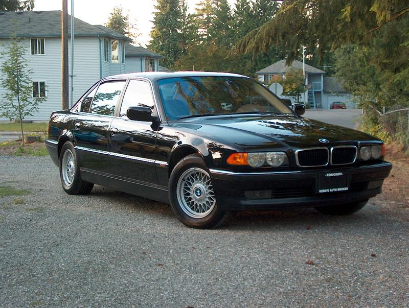Black BMW 7 Series sedan, front three-quarter view on gravel lot