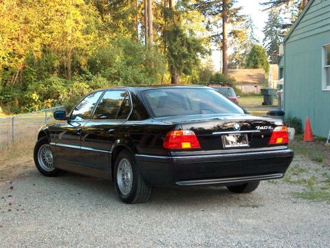 1999 BMW 7 Series - A black 1999 BMW 740iL is parked in a driveway with trees and a building in the background.