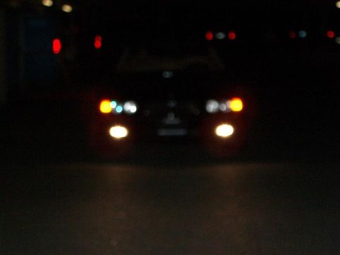 1999 BMW 7 Series - The front lights of a car are visible in the dark, with some bokeh effect from background lights.