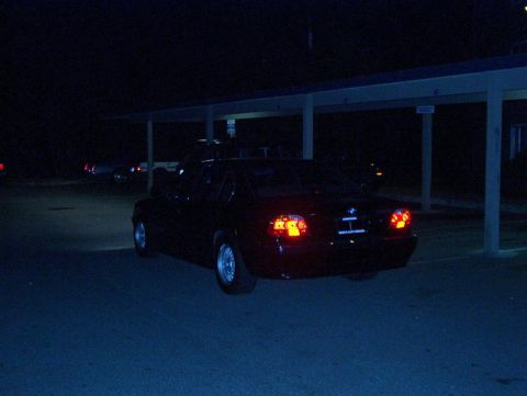 1999 BMW 7 Series - A black sedan is parked under a covered structure at night, its taillights glowing.