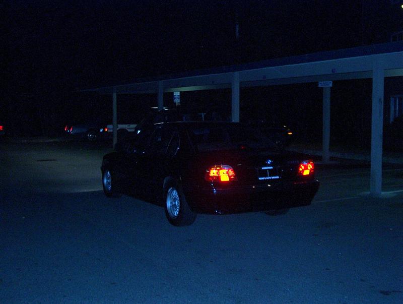 Rear view of a dark BMW sedan at night with lit taillights in a carport