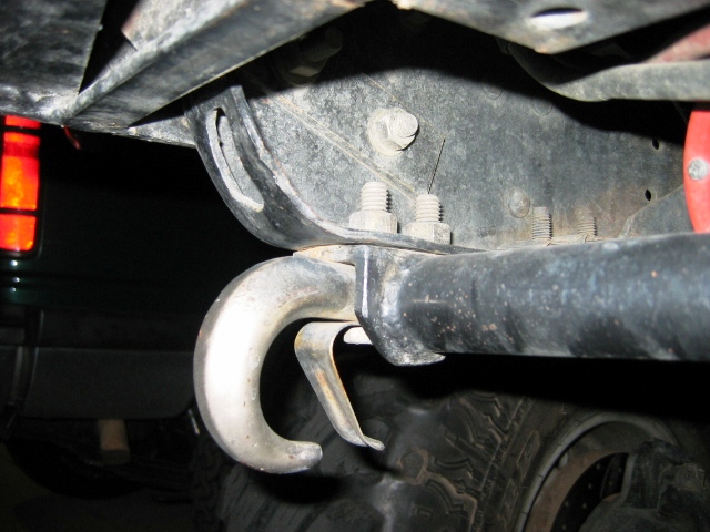 Silver tow hook bolted to black frame bracket under a truck, with exposed studs and tire nearby