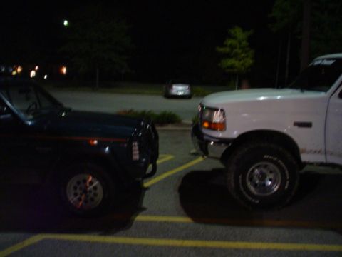 1993 Ford Bronco - Two trucks are parked facing each other in a dimly lit parking lot.