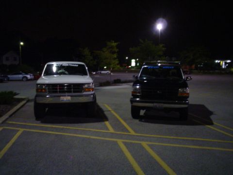 1993 Ford Bronco - Two Ford trucks are parked in a lot at night, with one white and one black vehicle visible.