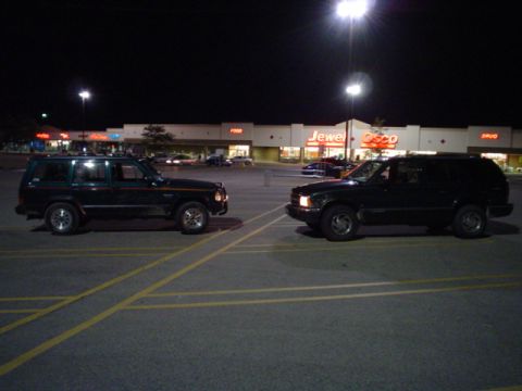 1993 Ford Bronco - Two SUVs are parked in a lot at night, with a supermarket visible behind them.