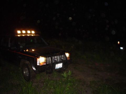 1993 Ford Bronco - A black Jeep Cherokee XJ equipped with a roof-mounted light bar is seen off-road at night.