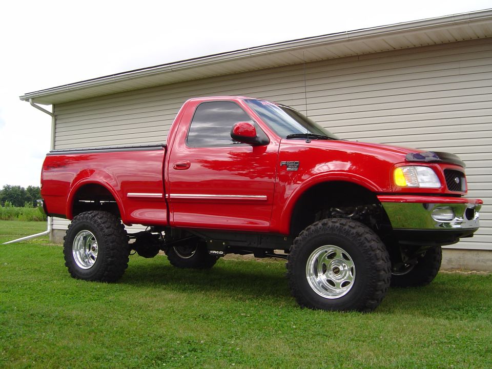 Red lifted Ford F-150 pickup truck parked on grass in front of a house