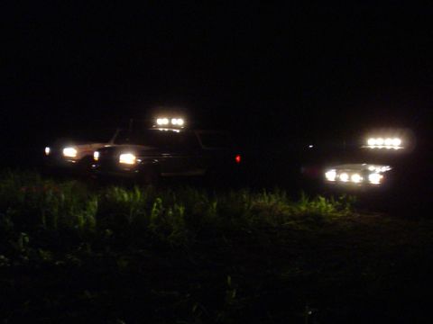 1993 Ford Bronco - Two SUVs are parked in tall grass at night, their off-road lights illuminating the darkness.