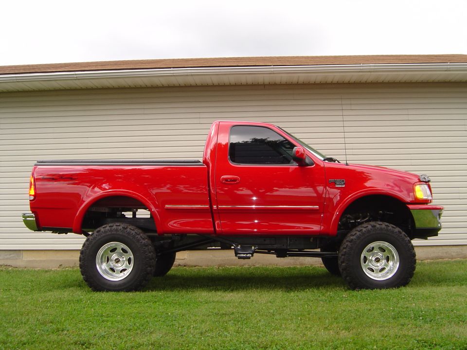 Red lifted regular-cab Ford F-150 pickup, passenger side profile on grass