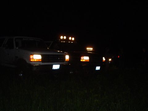 1993 Ford Bronco - Several trucks are parked in a field at night, illuminated by their headlights and light bars.