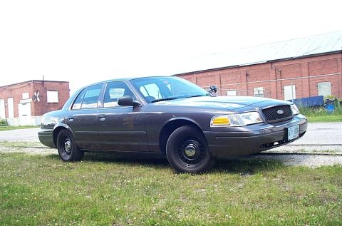 2001 Ford Crown Victoria - A dark gray 2001 Ford Crown Victoria is parked on a grassy area next to a brick building.