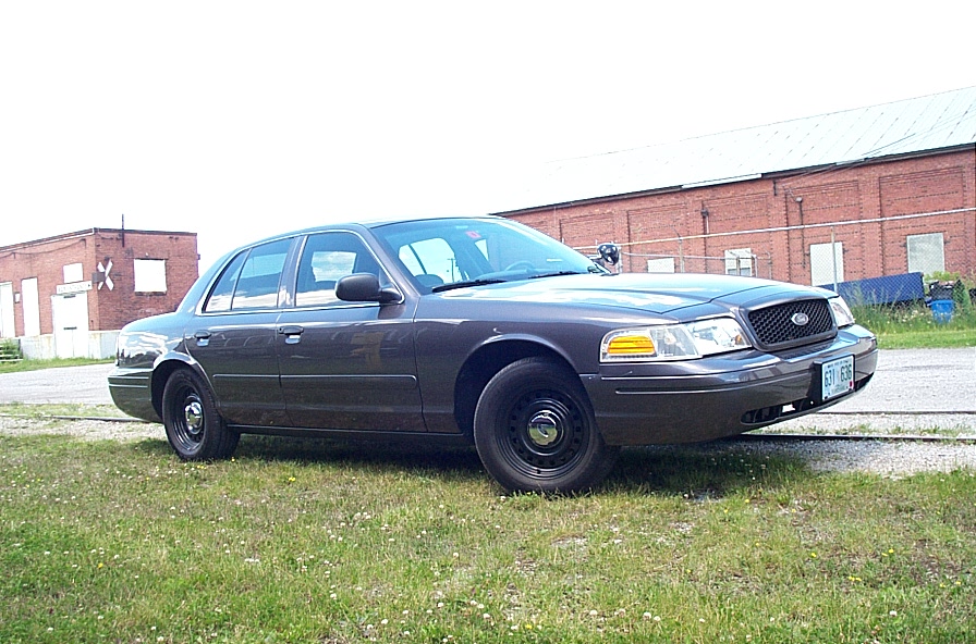Dark gray 2001 Ford Crown Victoria parked on grass, front quarter view. Black steel wheels, some dirt on front bumper