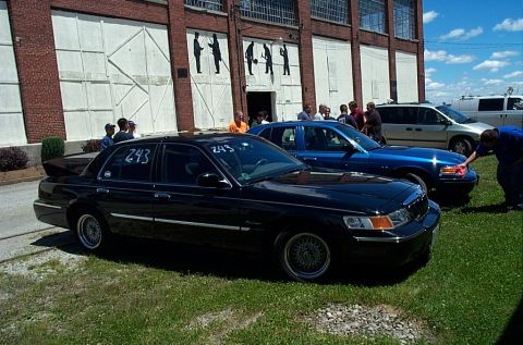 2001 Ford Crown Victoria - A black Mercury Grand Marquis sedan with chrome wire-spoke wheel covers and "243" soaped on its windows sits on grass at an outdoor car eve…