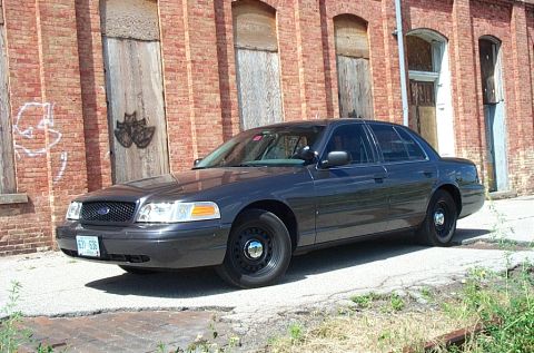 2001 Ford Crown Victoria - Grey unmarked Ford Crown Victoria Police Interceptor parked at a front three-quarter angle on cracked pavement in front of an abandoned bri…