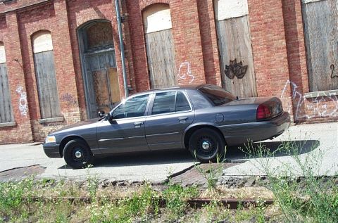 2001 Ford Crown Victoria - Side view of a 2001 Ford Crown Victoria parked near an old brick building with graffiti.