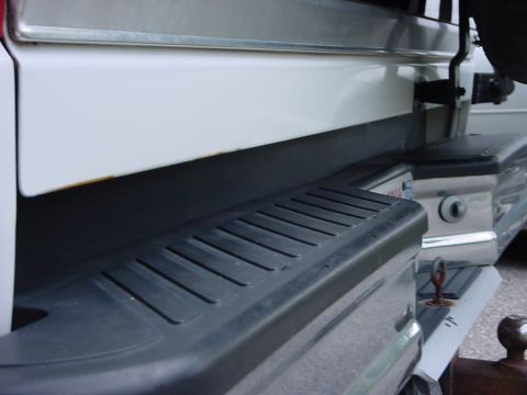 1989 Ford Bronco - Close-up of the rear bumper and tailgate area of a white SUV, showing a step and tow hitch. The image includes a watermark for SUPERMOTORS.…