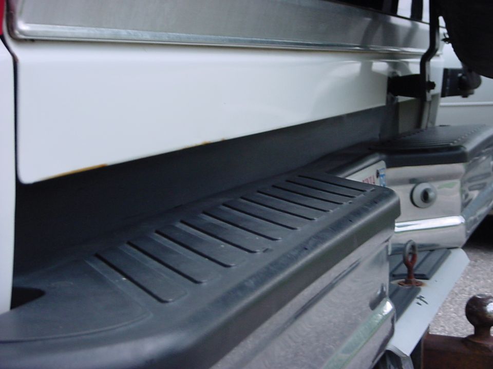 White SUV rear bumper with step and tow hitch. Watermark reads SUPERMOTORS.NET