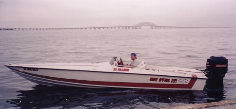 1994 Ford Bronco - A speed boat with a man at the helm is on the water, with a long bridge in the background.