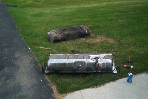 1985 Ford LTD Crown Victoria - Two automotive fuel tanks laid out on a lawn beside a driveway during a fuel pump replacement: a rusty, dirt-caked original tank in the bac…