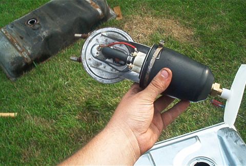 1985 Ford LTD Crown Victoria - Person holds a fuel pump and sending-unit assembly outdoors next to an old metal fuel tank on grass.
