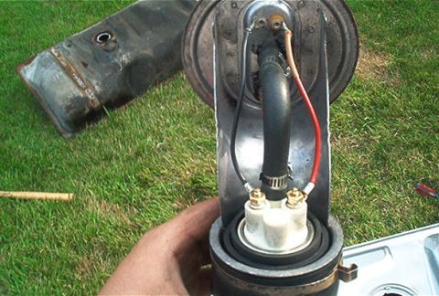 1985 Ford LTD Crown Victoria - Close-up of an in-tank fuel pump and sending unit assembly held up over a lawn, showing the pump canister with red and black power leads on…