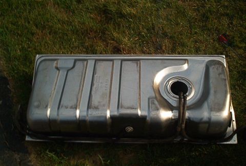 1985 Ford LTD Crown Victoria - A metal fuel tank is shown resting on grass, with visible stamped markings and hoses attached.