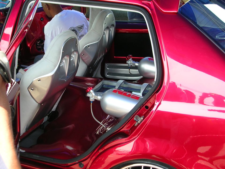 Custom red vehicle interior showing bucket seats and two nitrous oxide tanks mounted on the floor