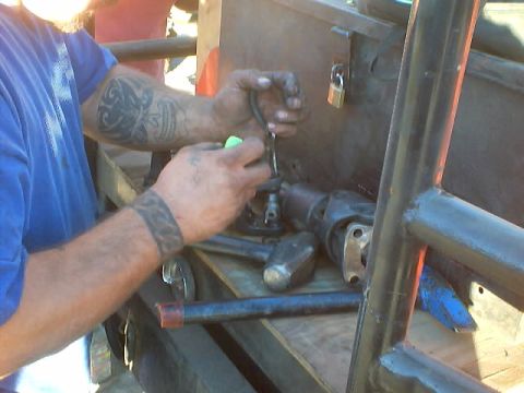 1976 Ford F-100 - Man works on vehicle drivetrain parts, including a driveshaft and U-joint.