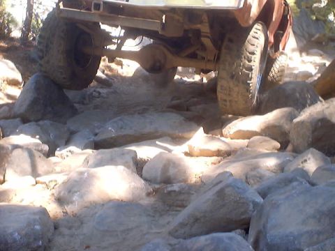 1976 Ford F-100 - Vehicle navigating a challenging rocky trail, showing its undercarriage and tires.