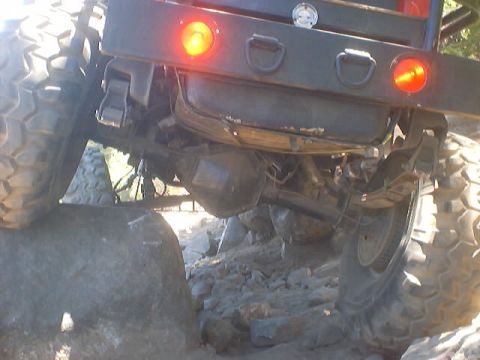 1976 Ford F-100 - The rear axle and massive tires of a truck are shown navigating a rocky terrain.